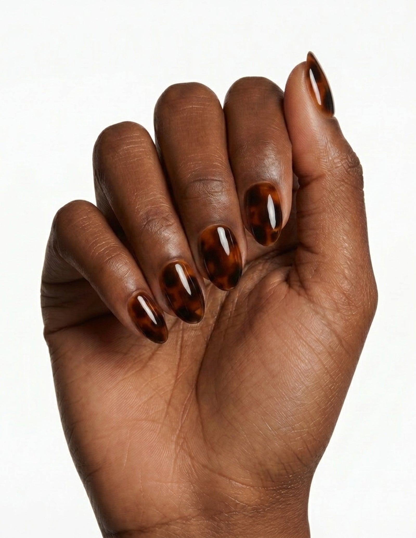 Tortoise press-on nails — Almond (extra-short), deep-skin hand, fingers curled