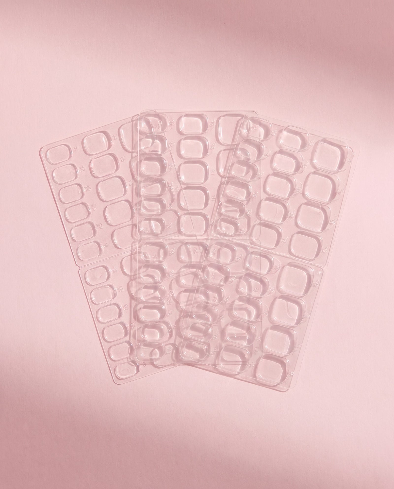 Three sheets of clear adhesive nail tabs fanned out flat, used to apply press-on nails without glue.
