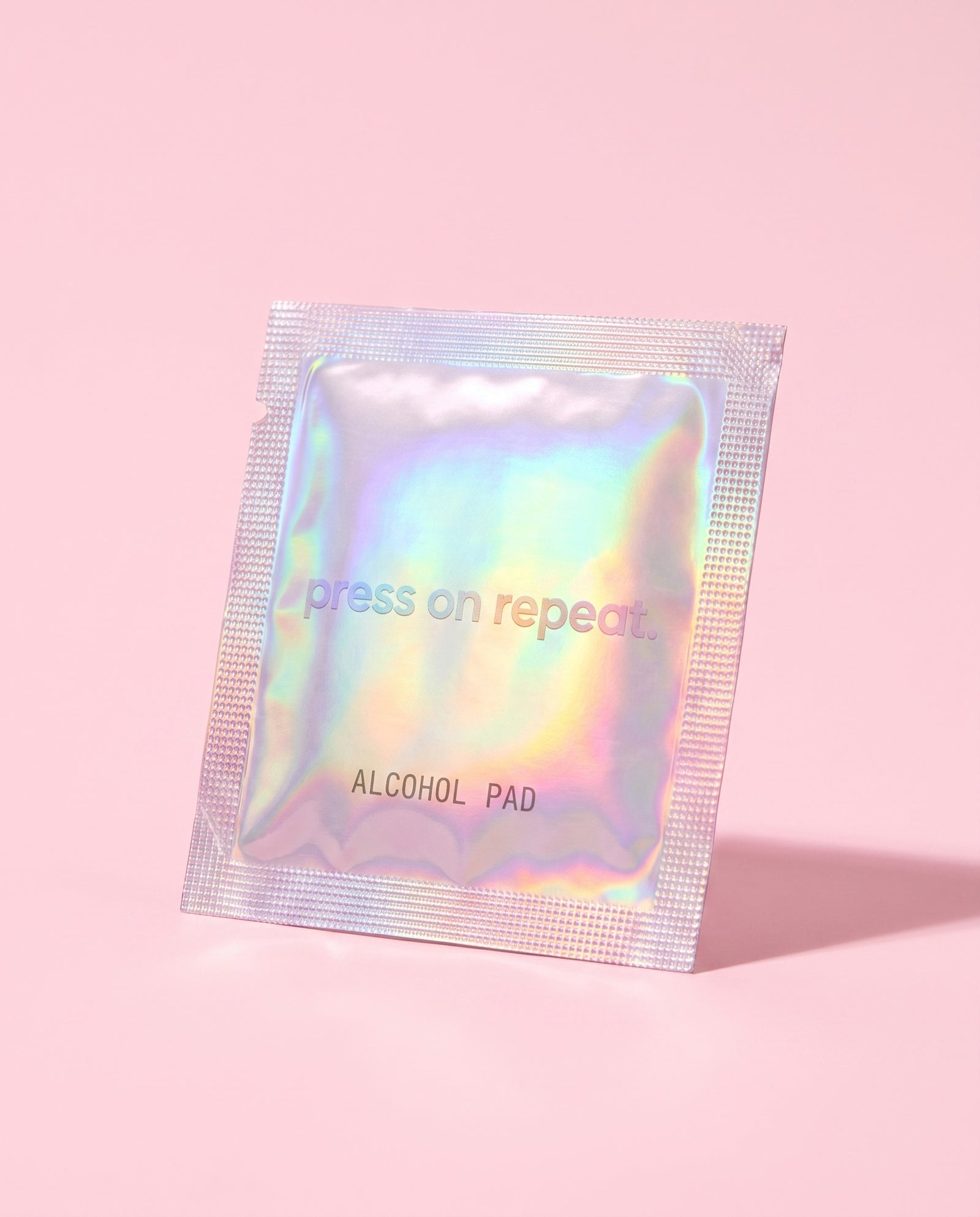 A single holographic foil alcohol pad sachet standing upright, printed with the Press On Repeat wordmark.