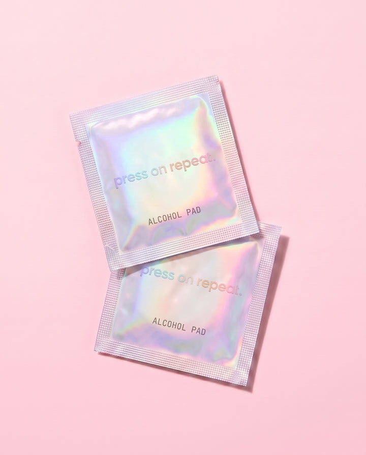 Two holographic foil alcohol pad sachets overlapping on a pink background.