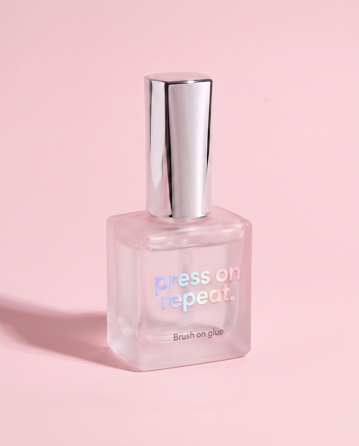Press On Repeat brush-on nail glue standing upright, frosted glass bottle with a chrome cap.