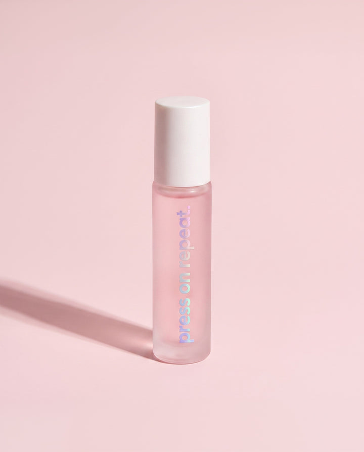Press On Repeat cuticle oil roll-on standing upright, frosted pink glass bottle with a white cap.