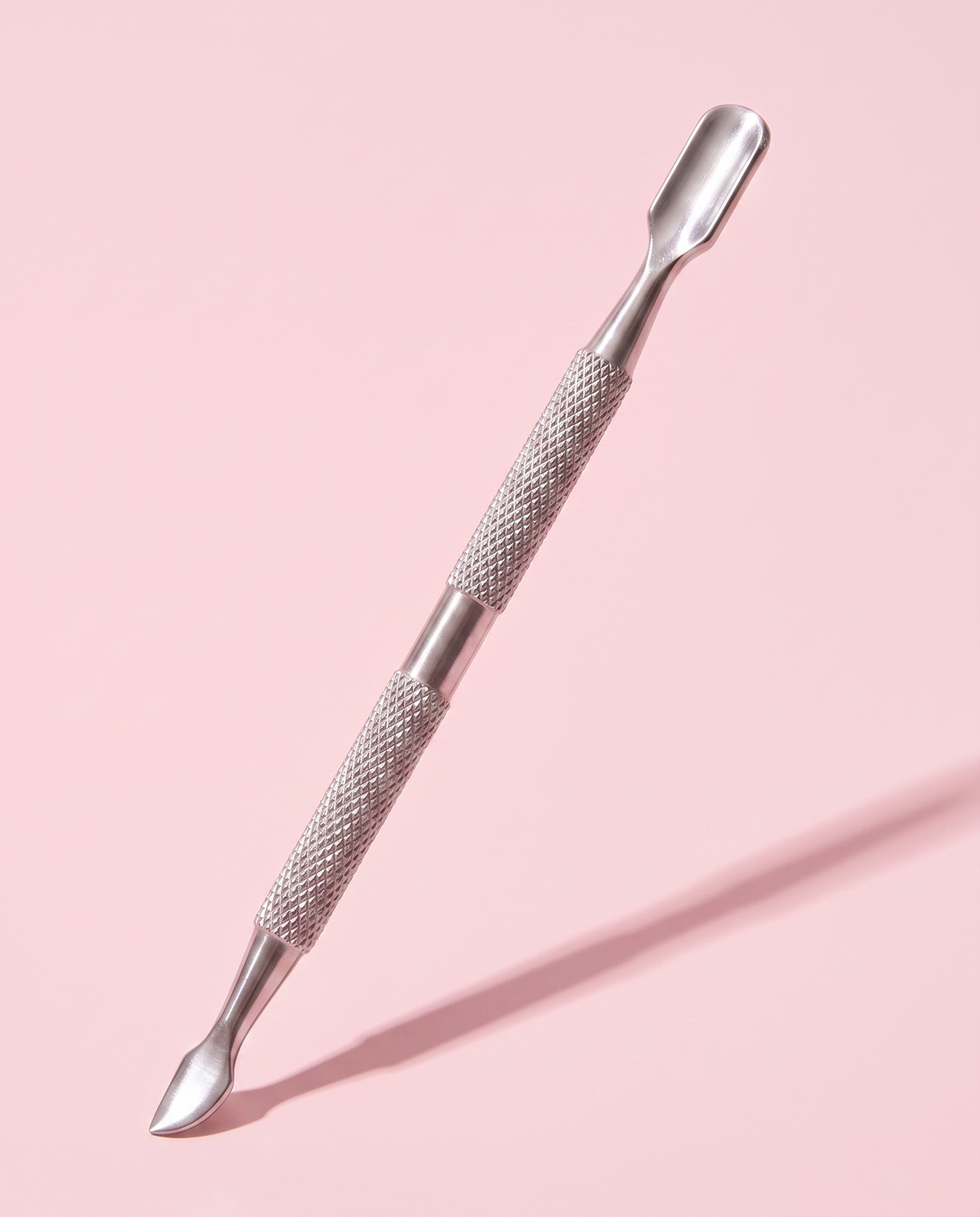 Press On Repeat stainless steel cuticle stick propped at an angle, flat pusher end raised.