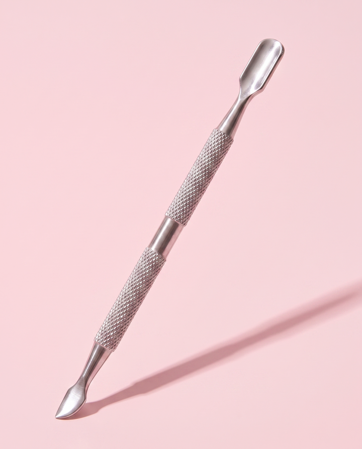 Press On Repeat stainless steel cuticle stick propped at an angle, flat pusher end raised.