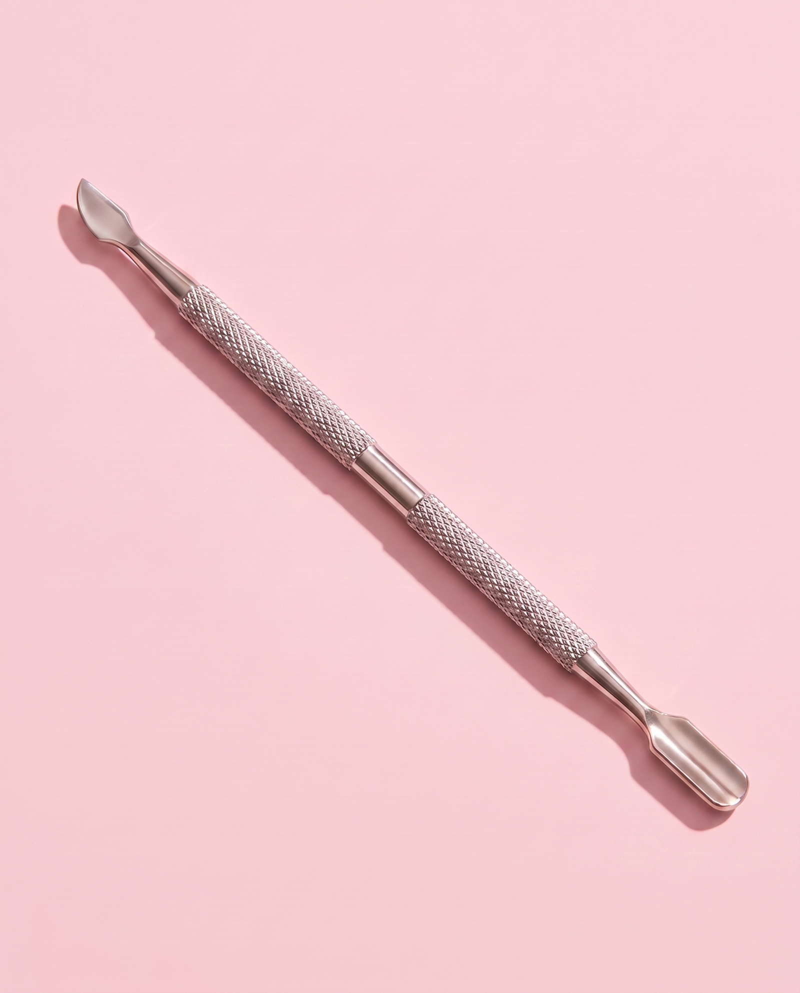 Stainless steel cuticle stick lying flat, curved cleanup tip toward the camera.