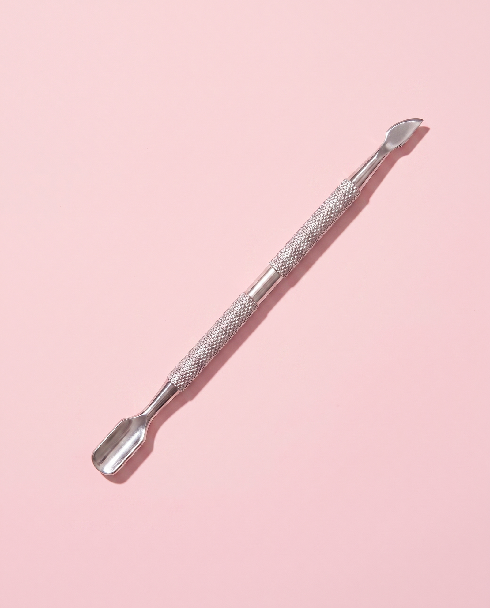 Stainless steel cuticle stick lying flat, flat pusher end toward the camera.