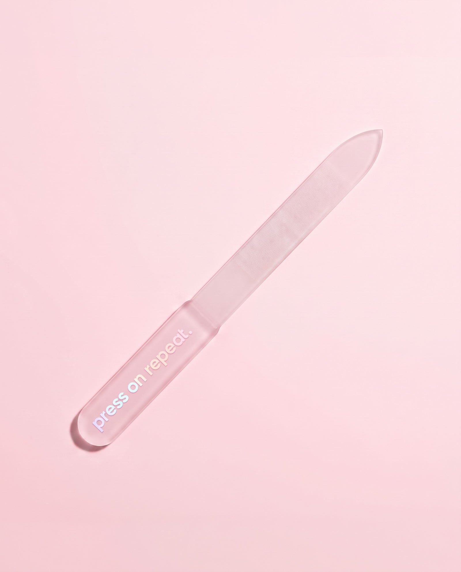 Frosted pink glass nail file leaning at an angle on a blush pink background.