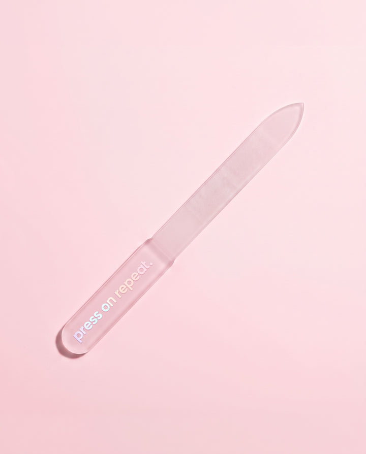 Frosted pink glass nail file leaning at an angle on a blush pink background.