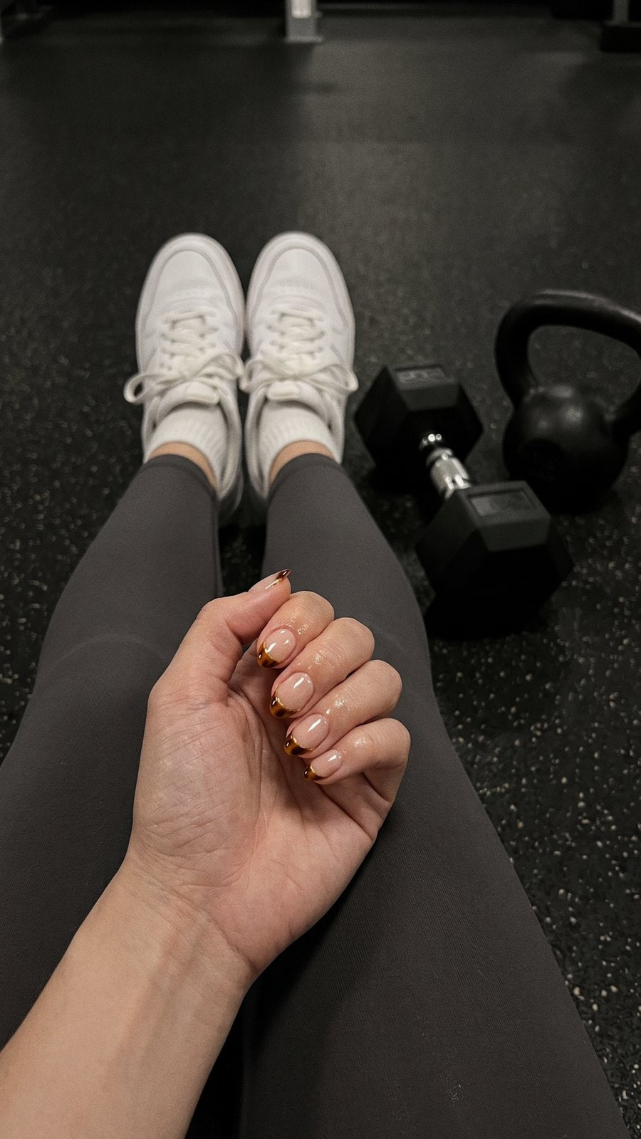 Looking down at the gym floor past a dumbbell and trainers, hands clasped with the set still on.